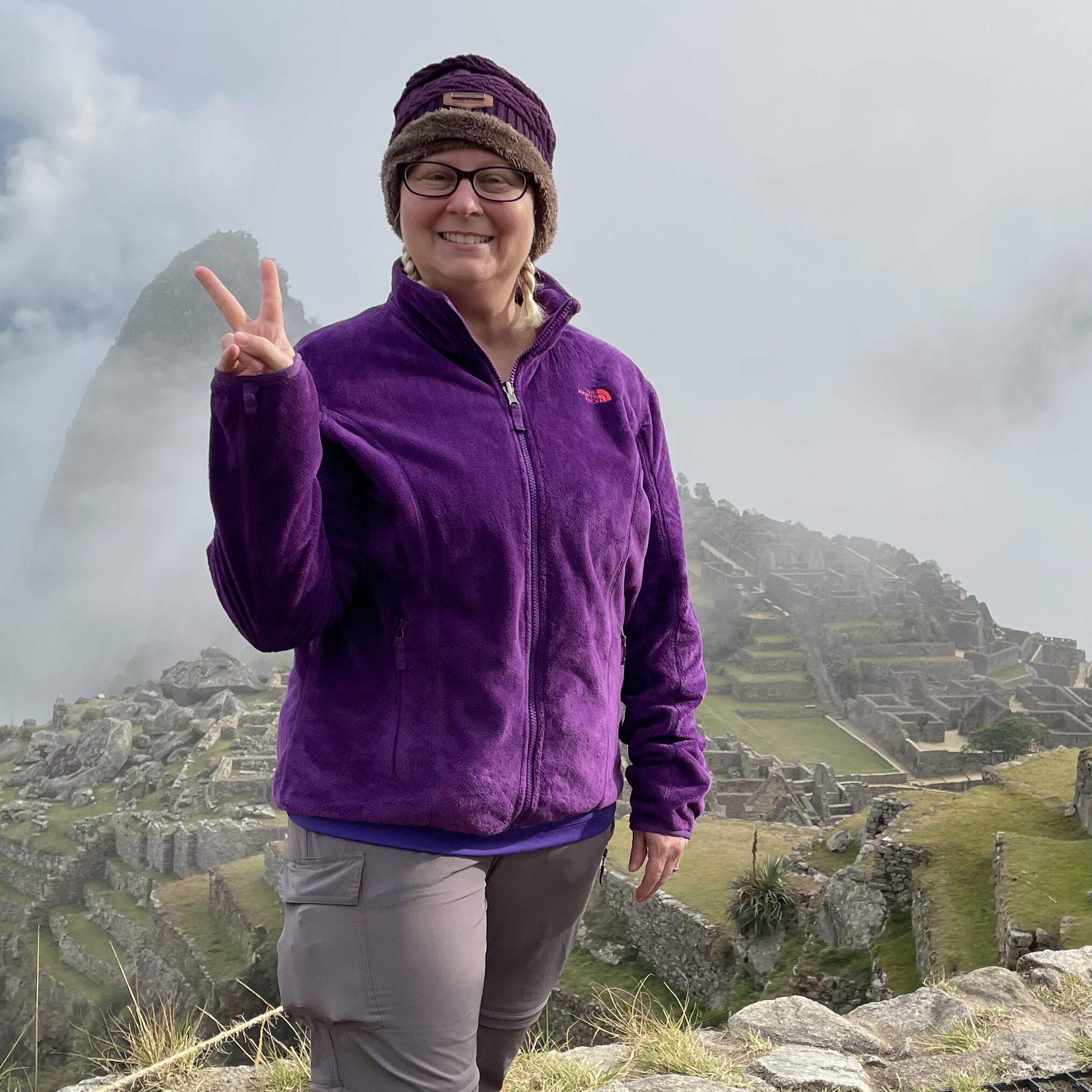 Female standing in front of Machu Picchu site holding up a peace sign while smiling.